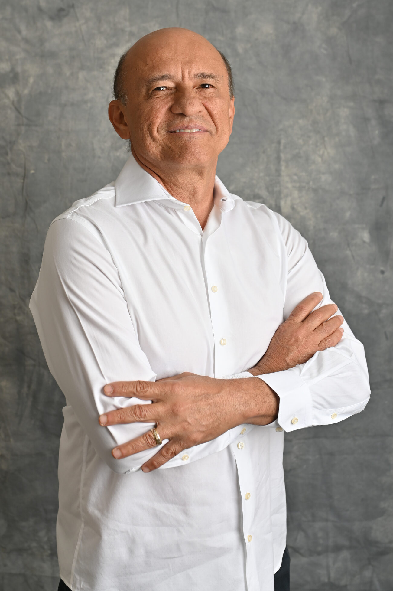 Livio Luciano, de camisa branca e braços cruzados, sorrindo